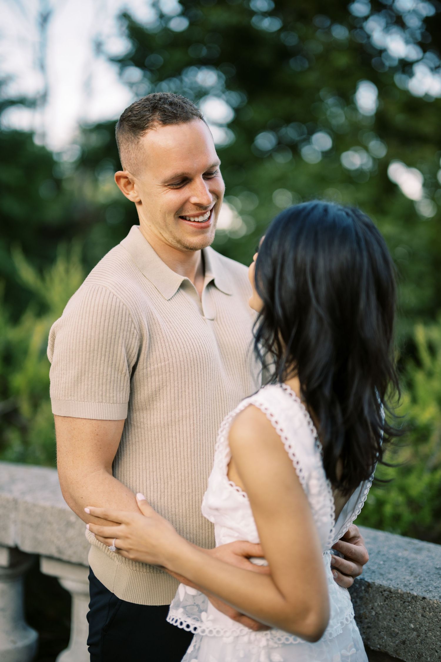 A joyful couple shares a tender moment together outdoors on a sunny day, with lush greenery in the background.