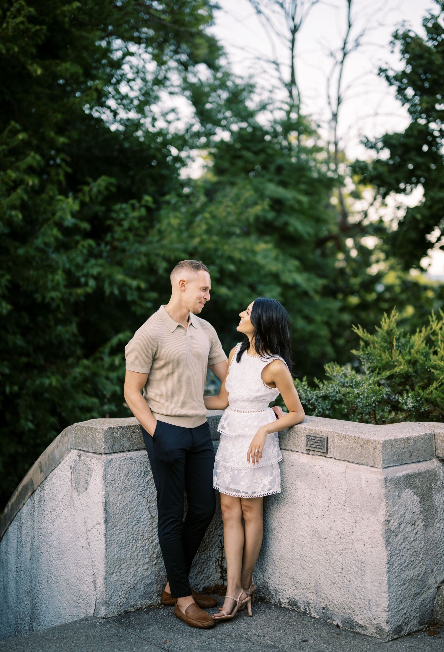 A romantic couple poses together on a stone overlook surrounded by lush greenery.