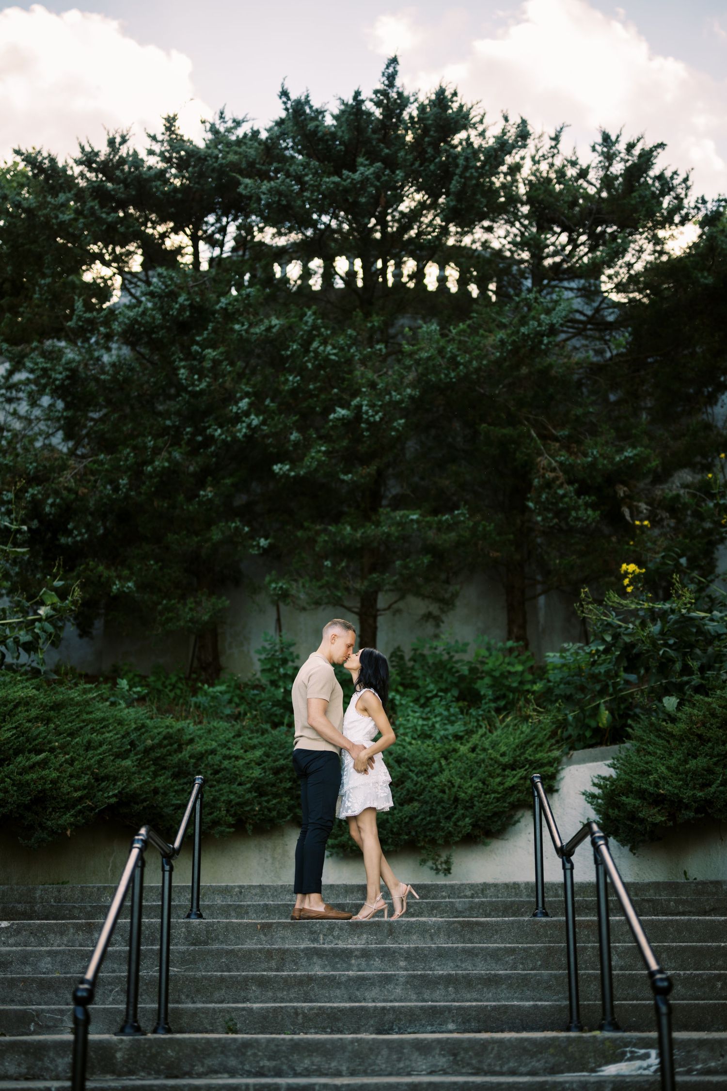 A romantic moment captured on stone steps surrounded by lush greenery at sunset.