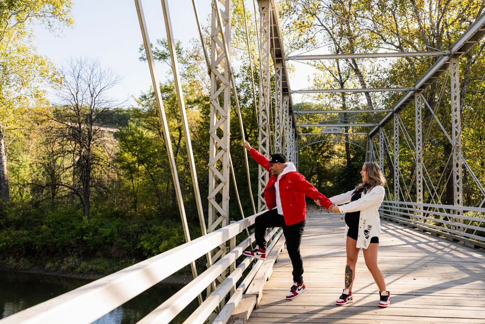 Two people stretch together on a scenic metal bridge surrounded by autumn foliage.