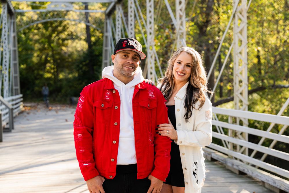 A couple poses together on a rustic metal bridge during a sunny autumn day.