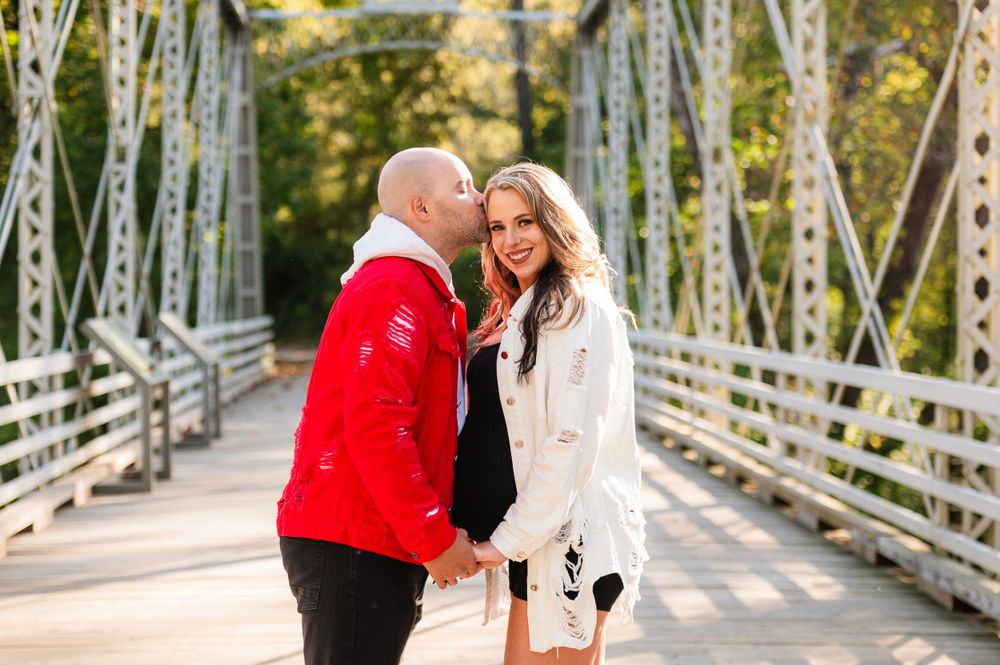 Two people hold hands while standing on a metal bridge, one wearing red and one in white.