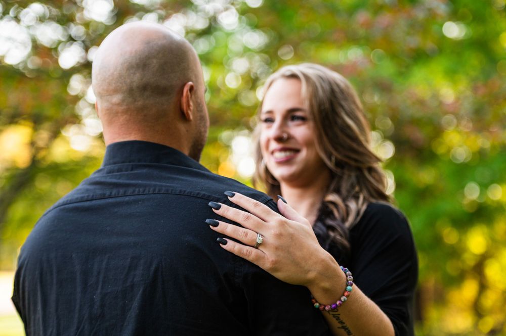 A couple shares a joyful outdoor moment in front of autumn foliage with soft bokeh lighting effects.