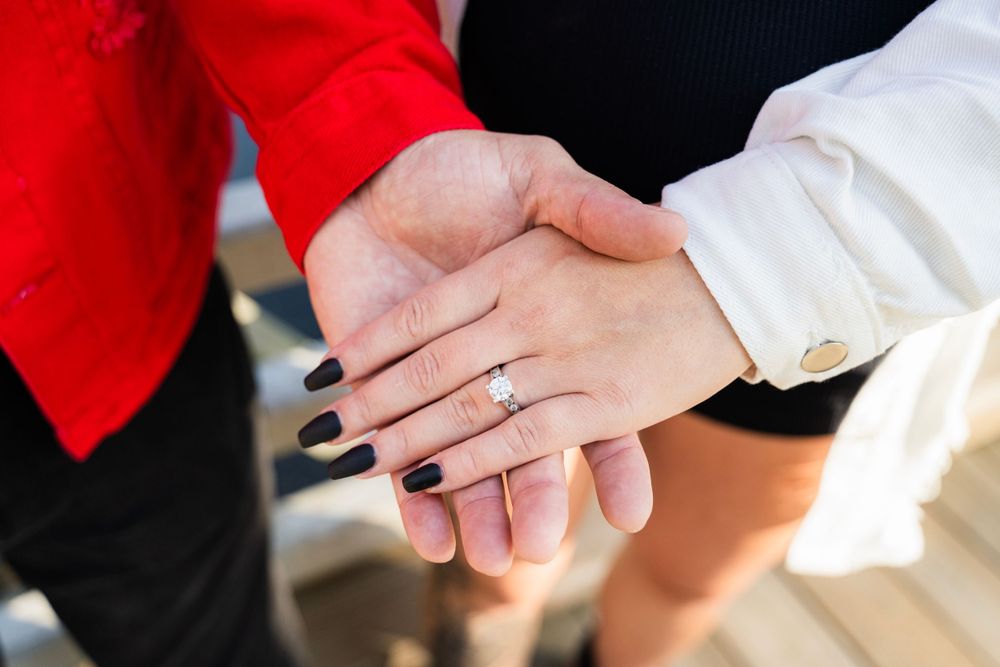 Close up of hands showing off engagement ring with a sparkly diamond solitaire against red and white clothing.