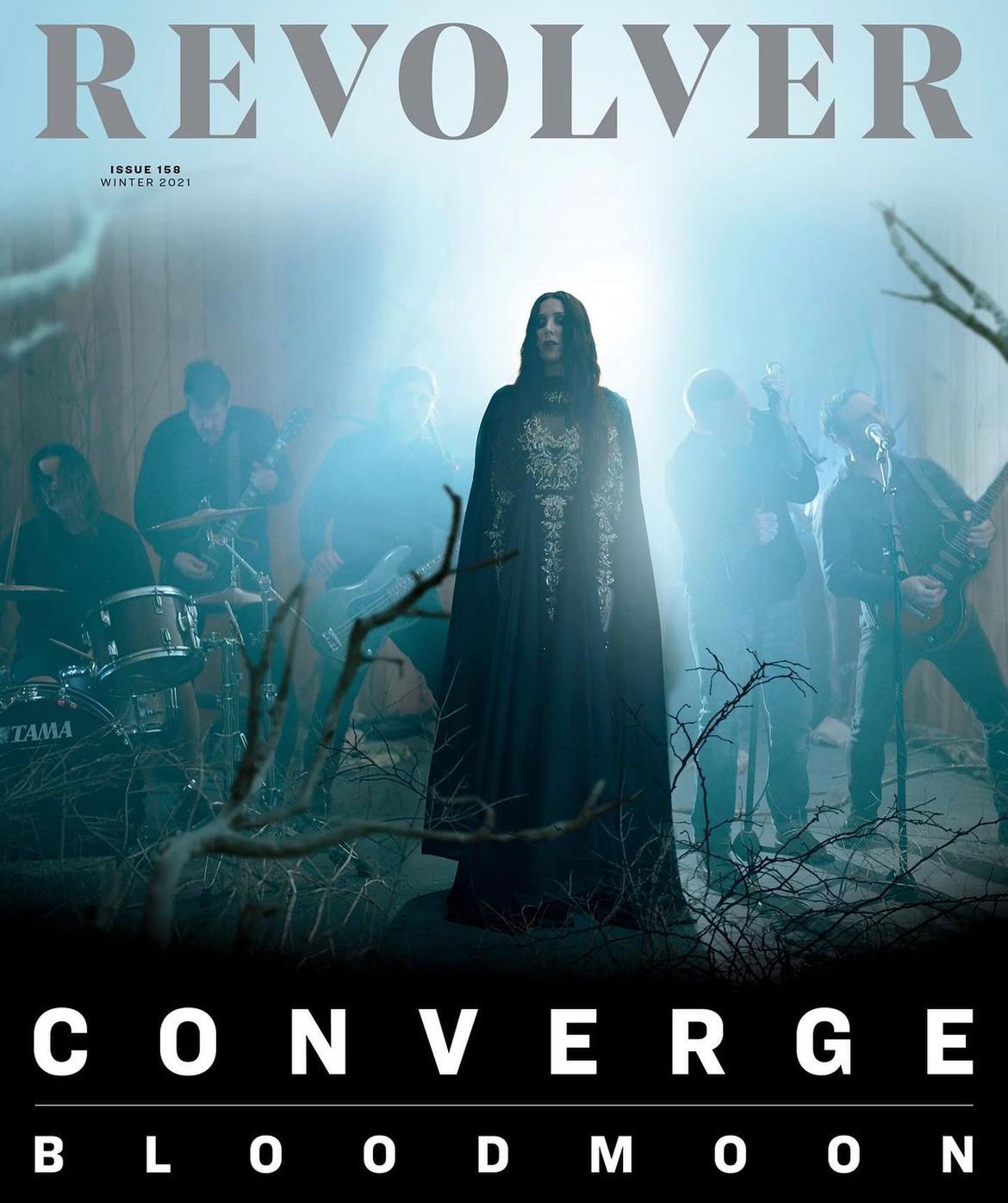 Moody band photo featuring hooded figure and musicians performing in misty forest setting.