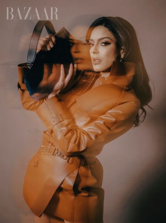 Fashion editorial features model in tan leather trench coat against warm tinted background.