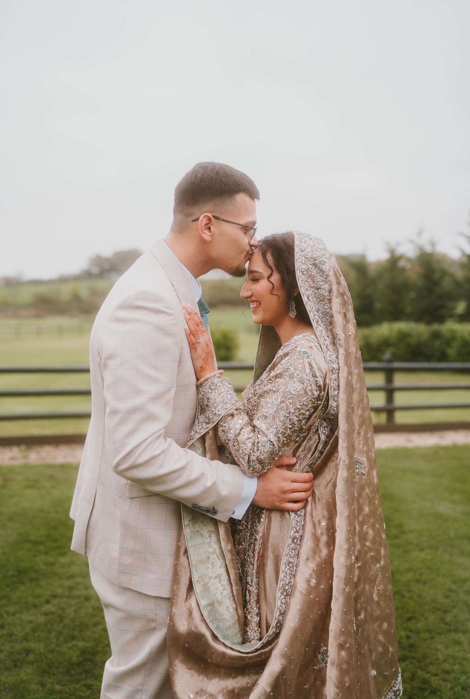 A tender moment between newlyweds outdoors with a pastoral background.