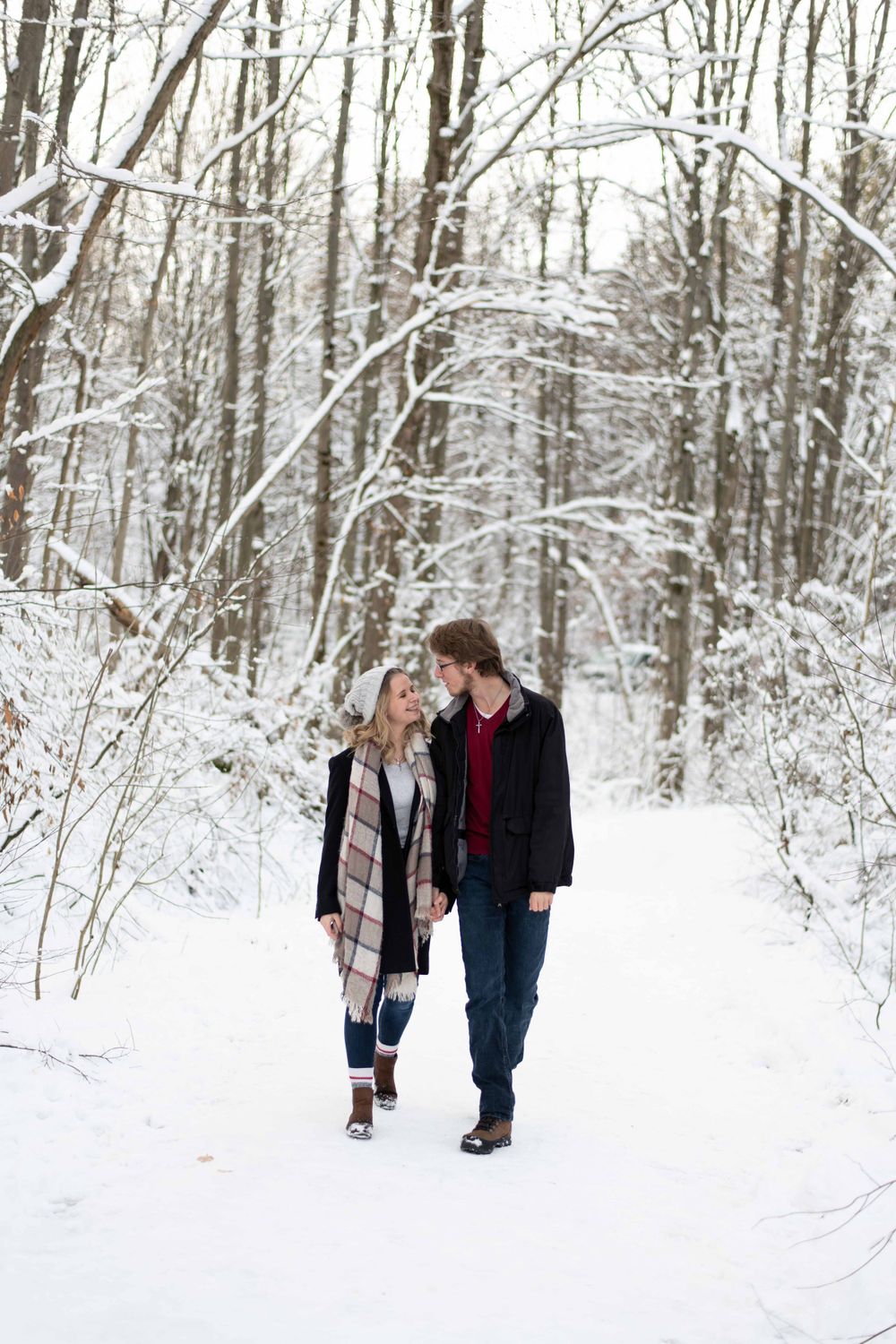 A couple walks together on a snowy path through a winter forest covered in fresh white snow.