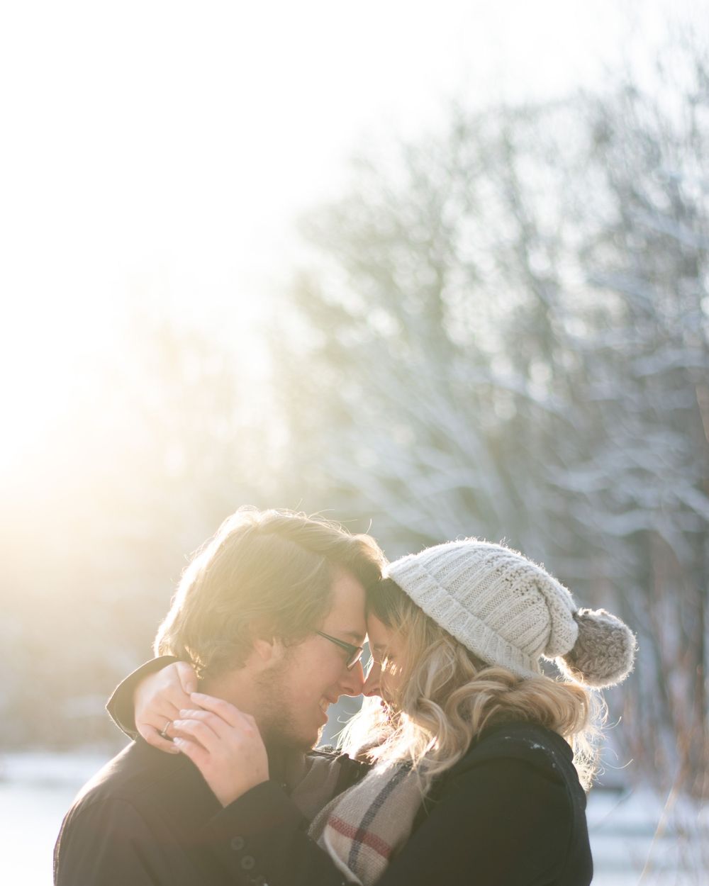 An intimate closeup of a couple in winter wear sharing a tender moment in golden sunlight.