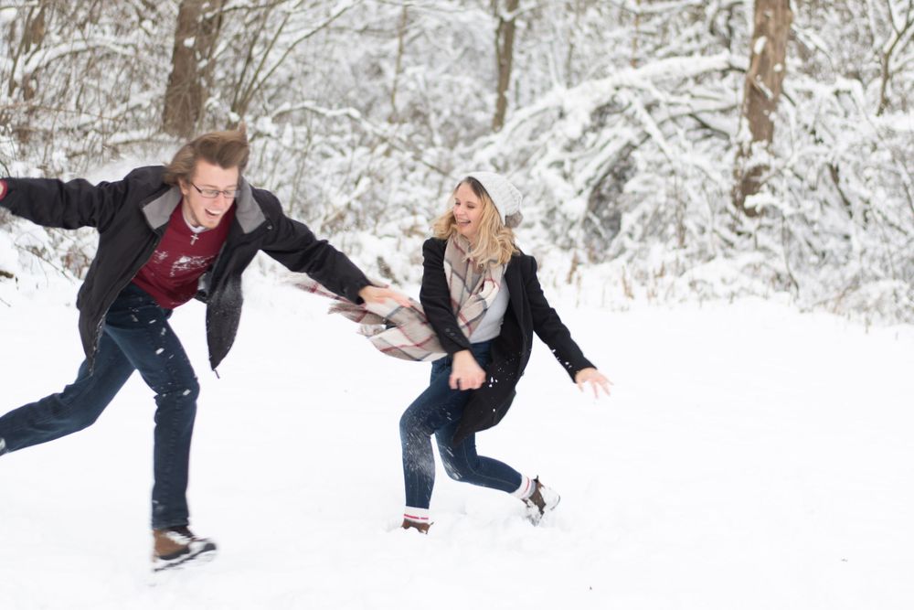 Two people playfully running and throwing snow in a snow-covered forest setting.