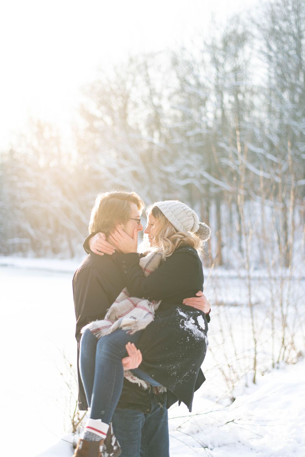 An intimate winter moment shared between two people with sunlight streaming through snowy trees.