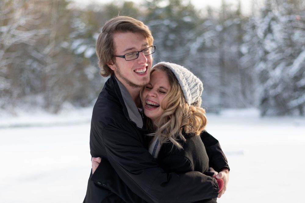 A joyful embrace shared between two people in winter coats against a snowy forest background.