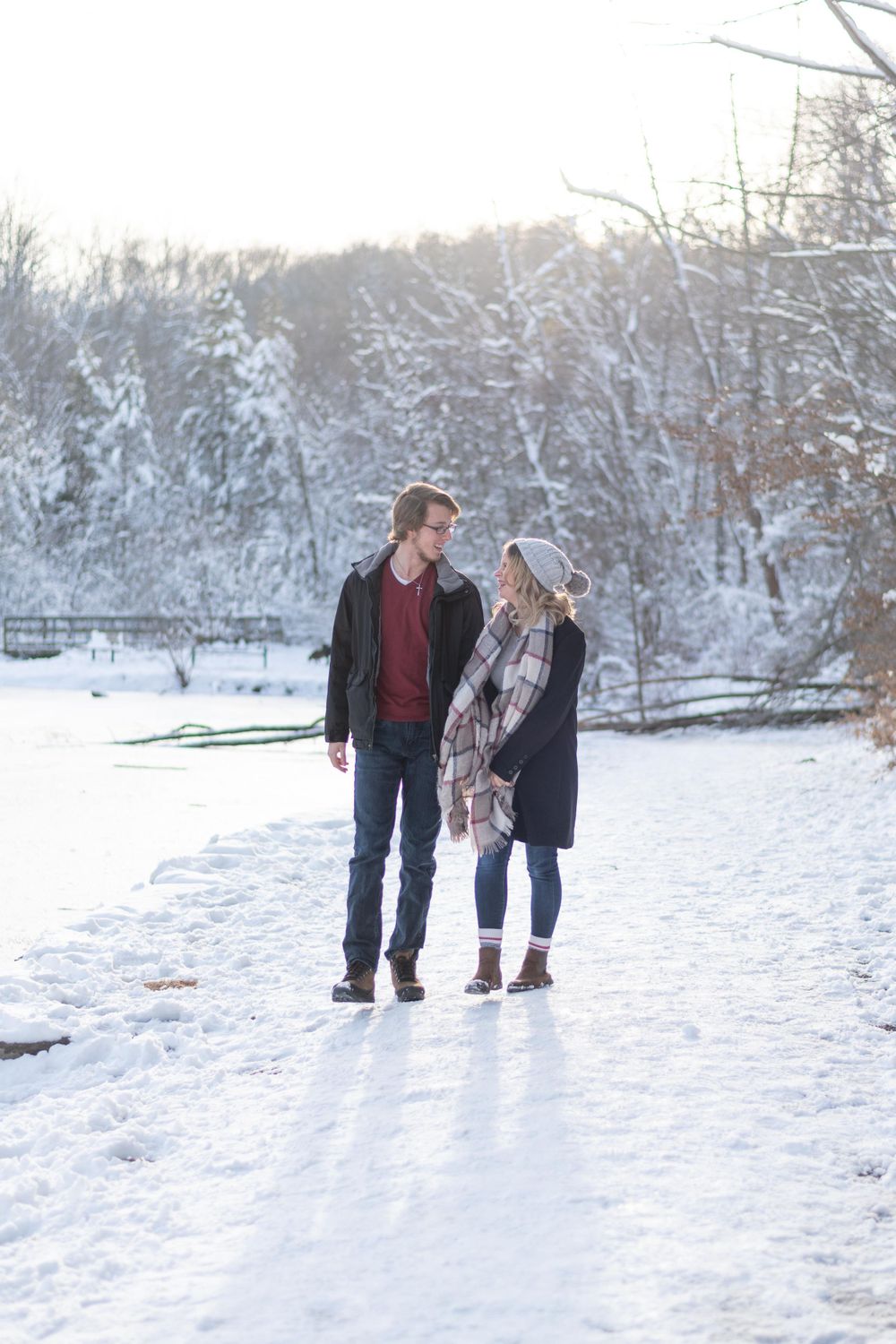 A couple walks together on a snow-covered path with winter trees in the background.