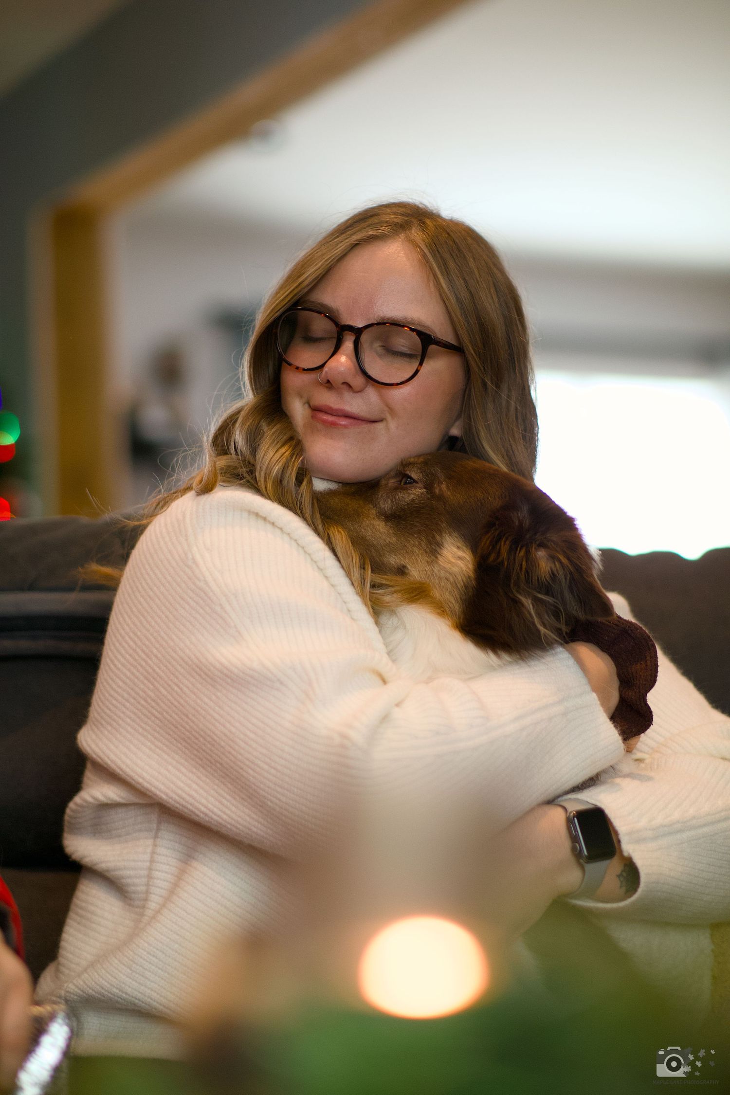 Someone in a white sweater hugging a brown dog while sitting on a couch.