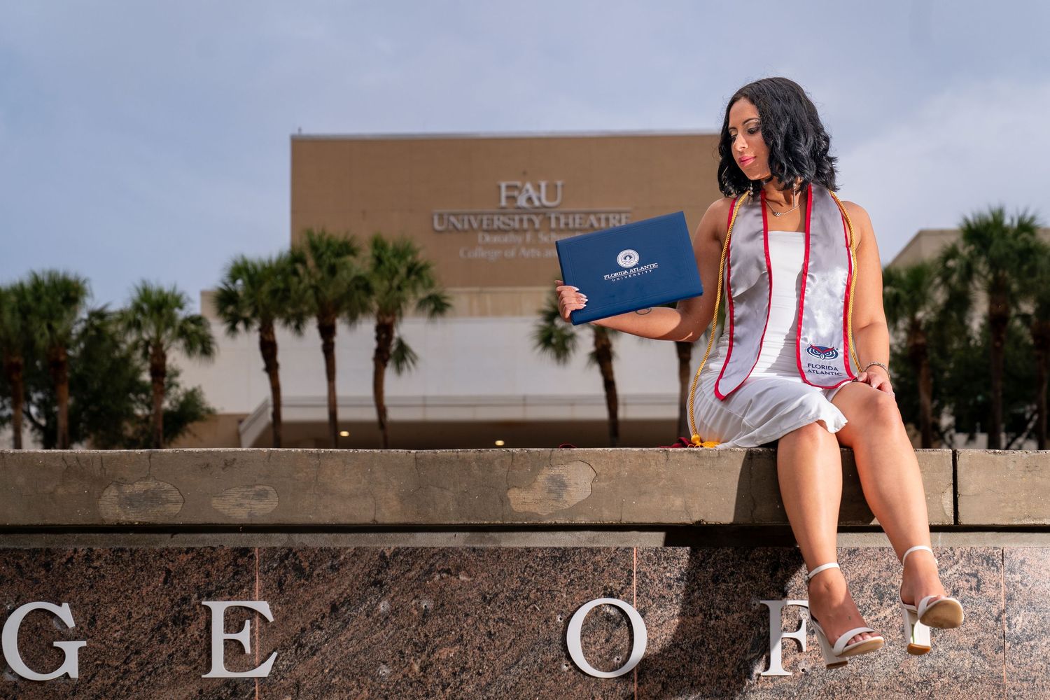 FAU graduate in cap and gown posing on campus with diploma, celebratory college graduation portrait by SRX Media Group in South Florida.