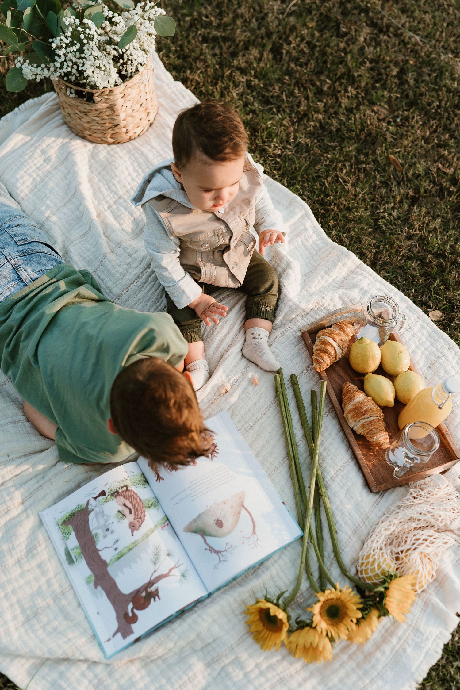 Picnic scene with books, sunflowers, and fruit on a white blanket.