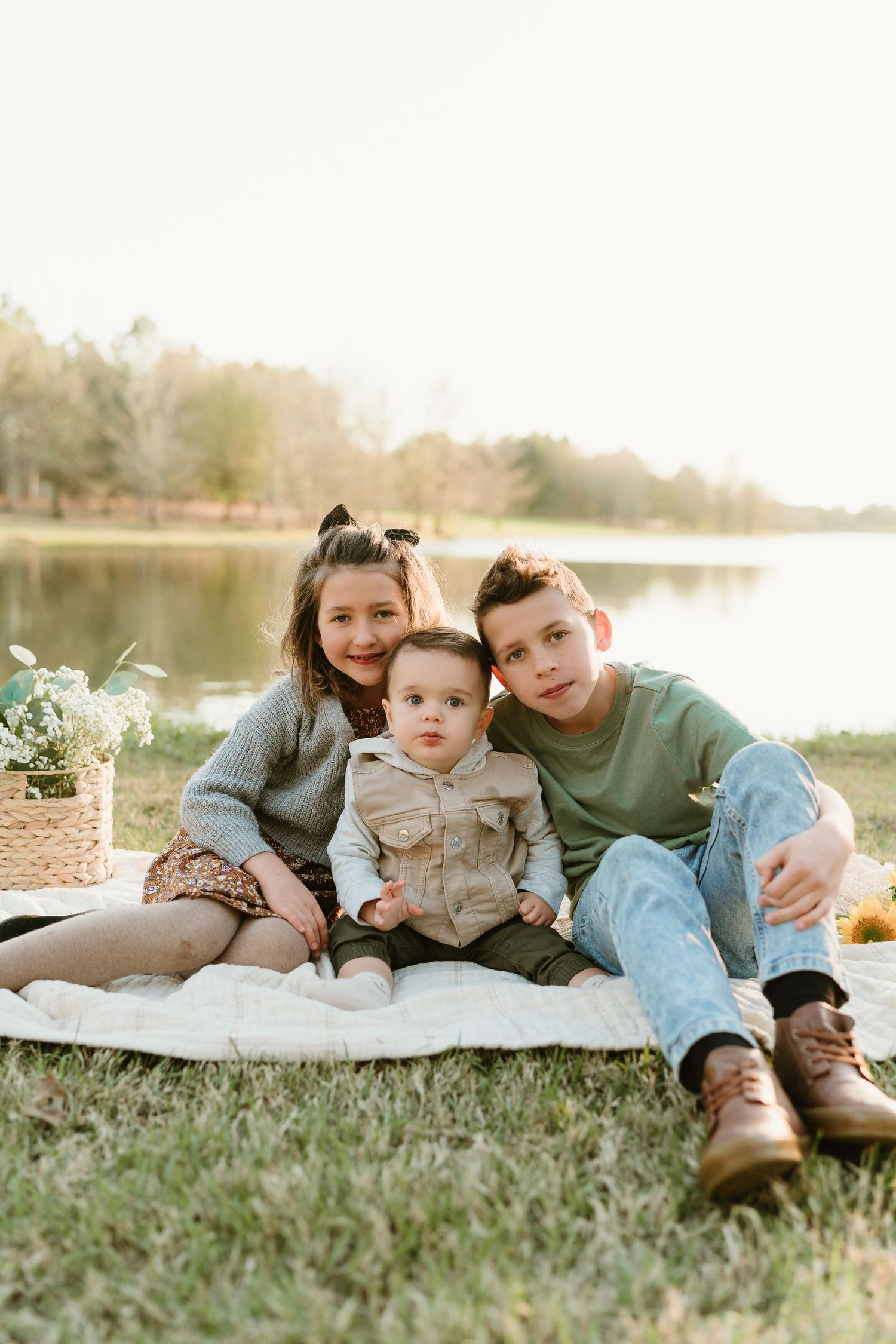 Family relaxing together on a blanket by the lake during sunset.