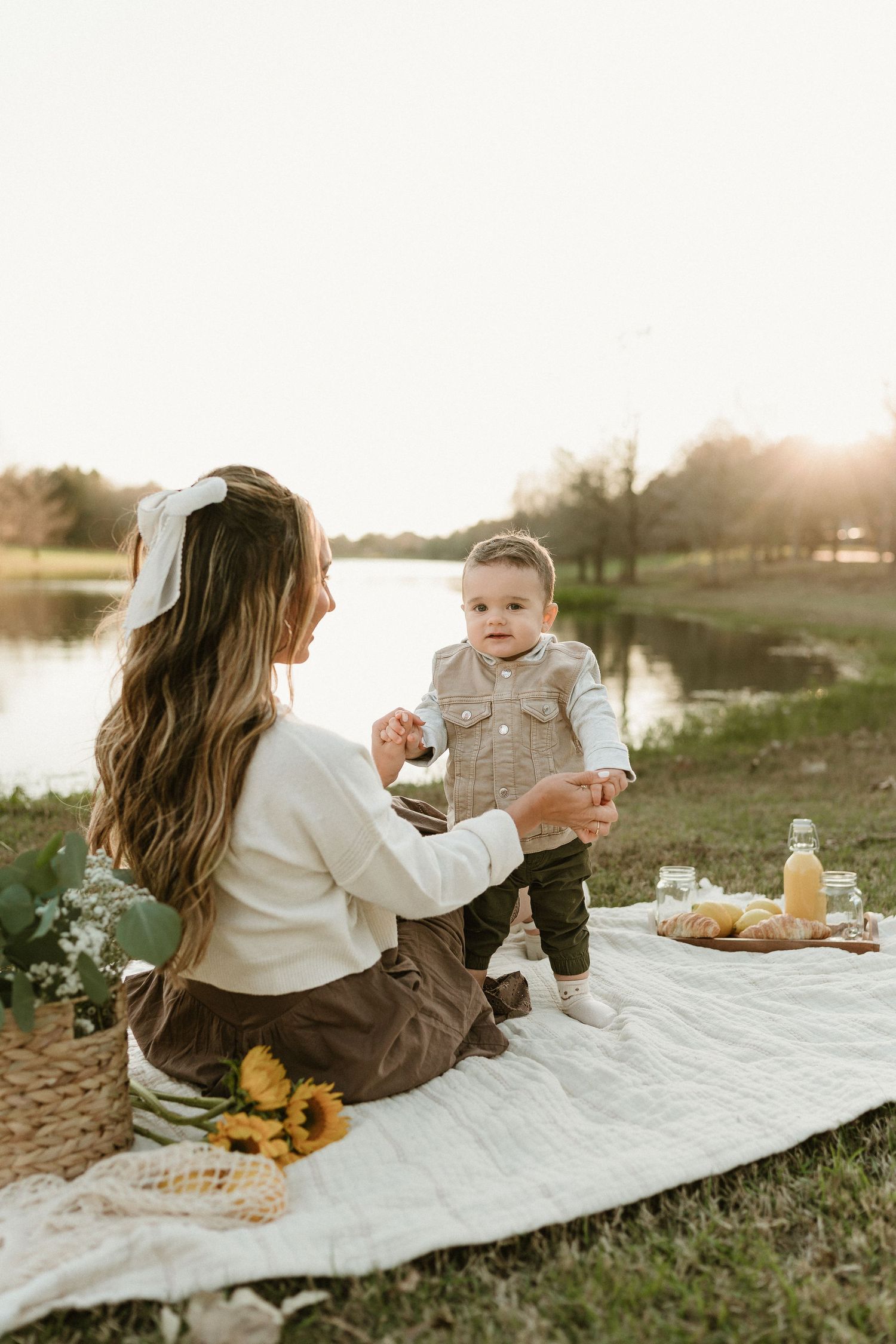 Outdoor picnic setup with fresh fruits and sunflowers by a peaceful lake during golden hour.