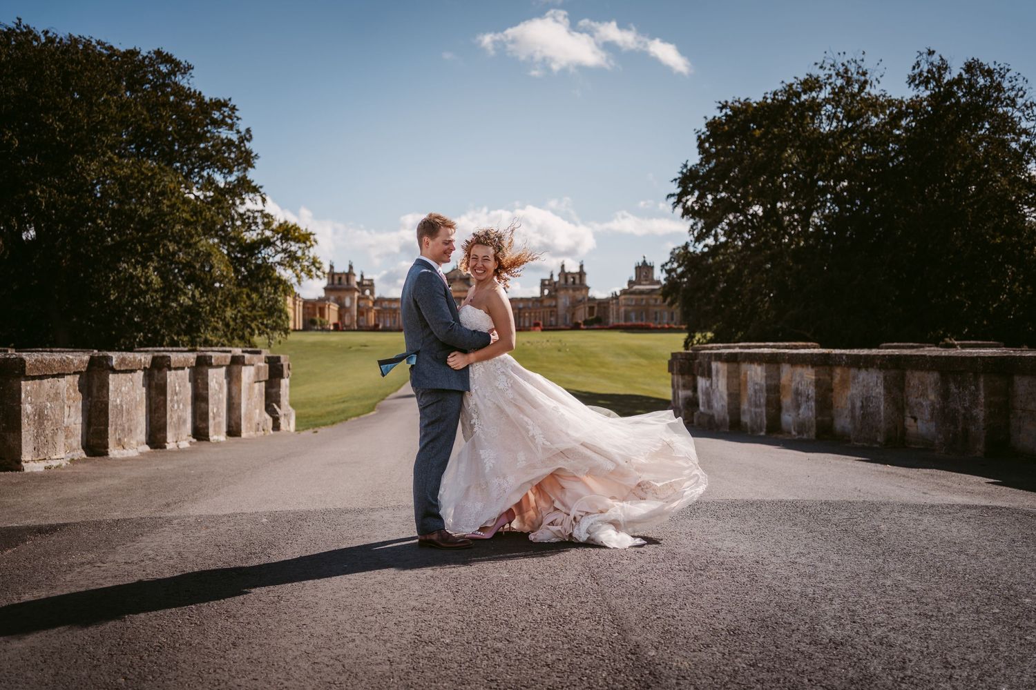 Blenheim Palace Wedding in Oxfordshire Cotswolds bride and groom with wind blowing hair and dress on bridge with palace backdrop Vicky Lewis