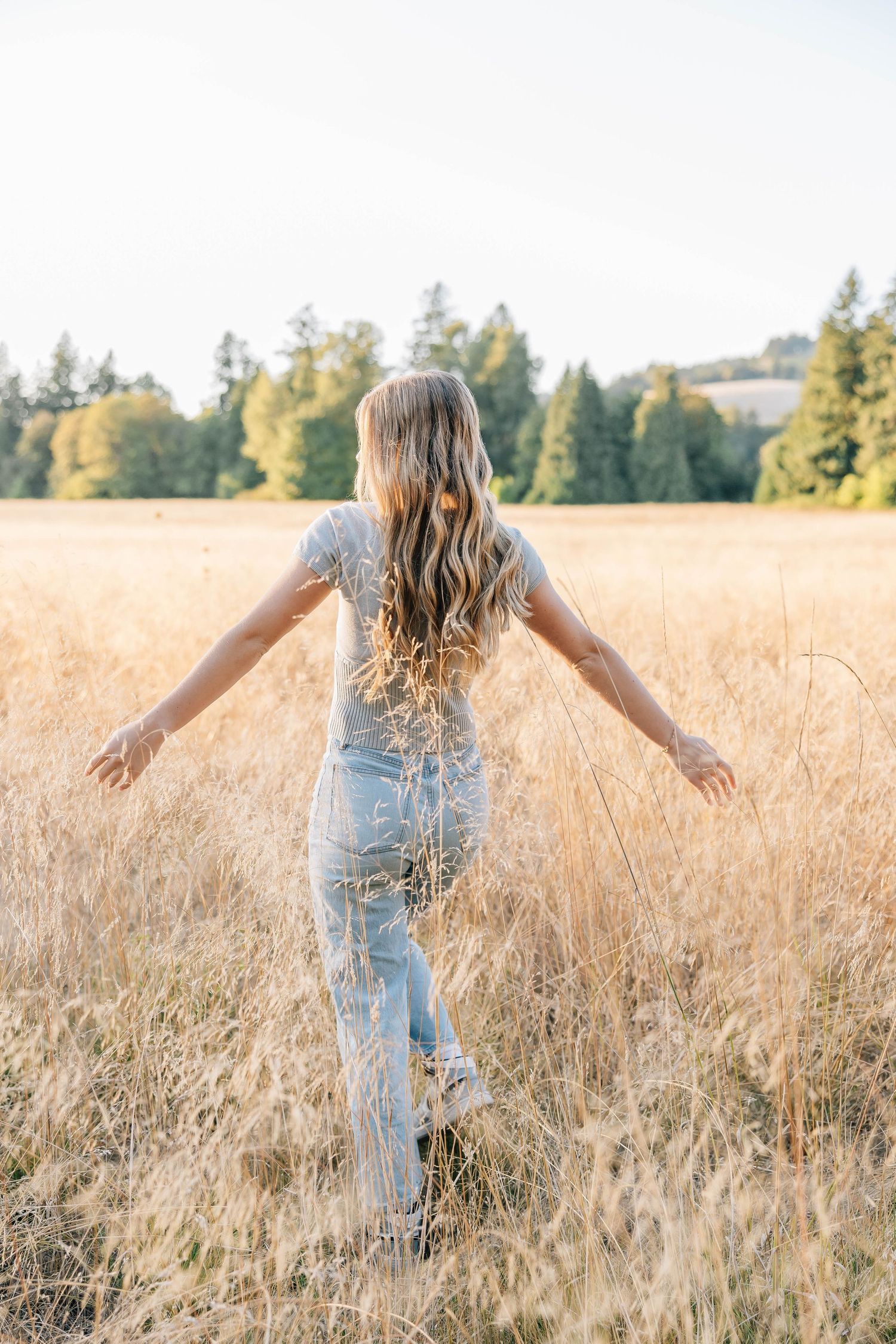 Blonde girl in floral dress walks through golden wheat field with arms outstretched.