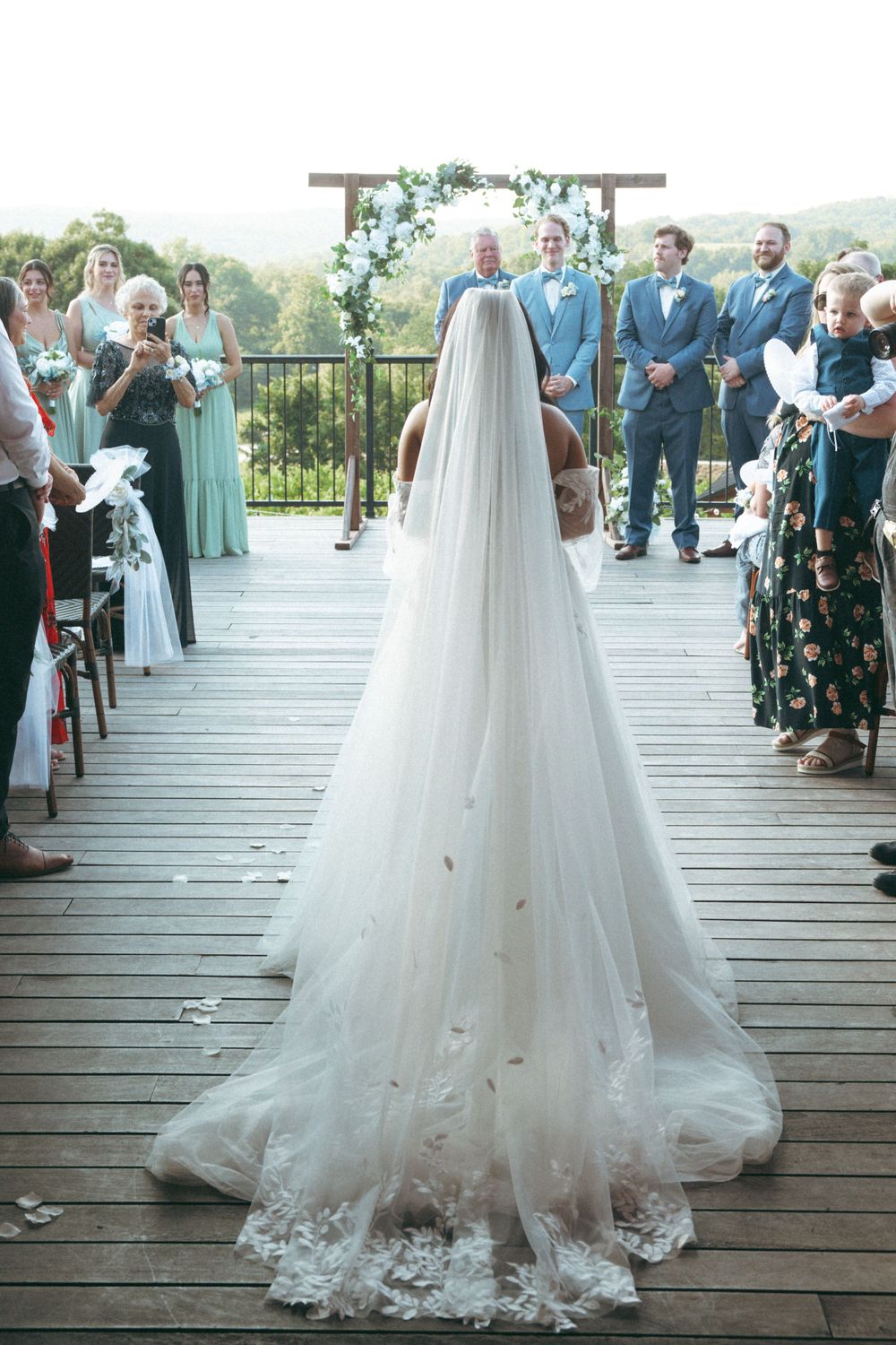 Long cathedral veil trails behind bride during outdoor ceremony with mountain views.