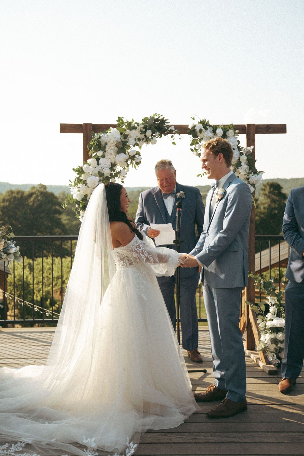 Outdoor wedding ceremony under floral arch with scenic mountain backdrop.