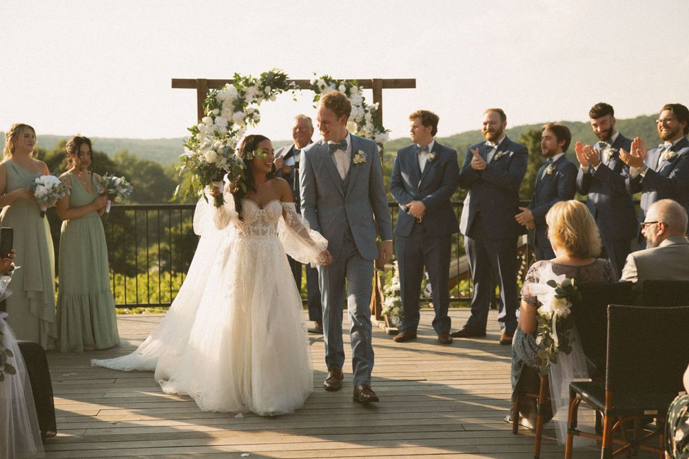 Wedding celebration on outdoor deck with guests seated and floral arch backdrop.