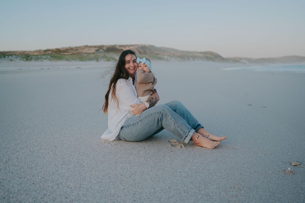 A young mother sits with her baby on the beach in blue hour - Bremer Bay