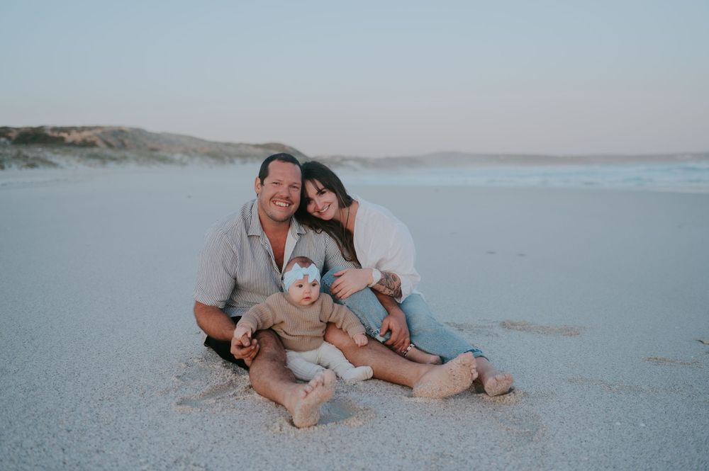 A young mother, father and their baby sit on the beach in blue hour - Bremer Bay