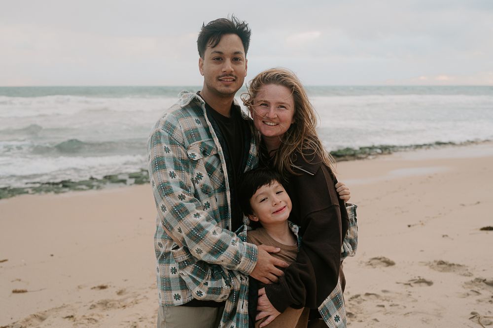 Mum, dad and young son hugging on Perth beach