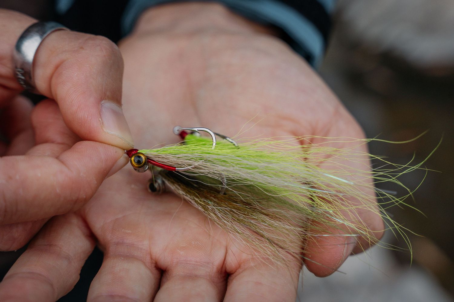 Close-up view of hands tying a green fishing fly with delicate thread and feathers.
