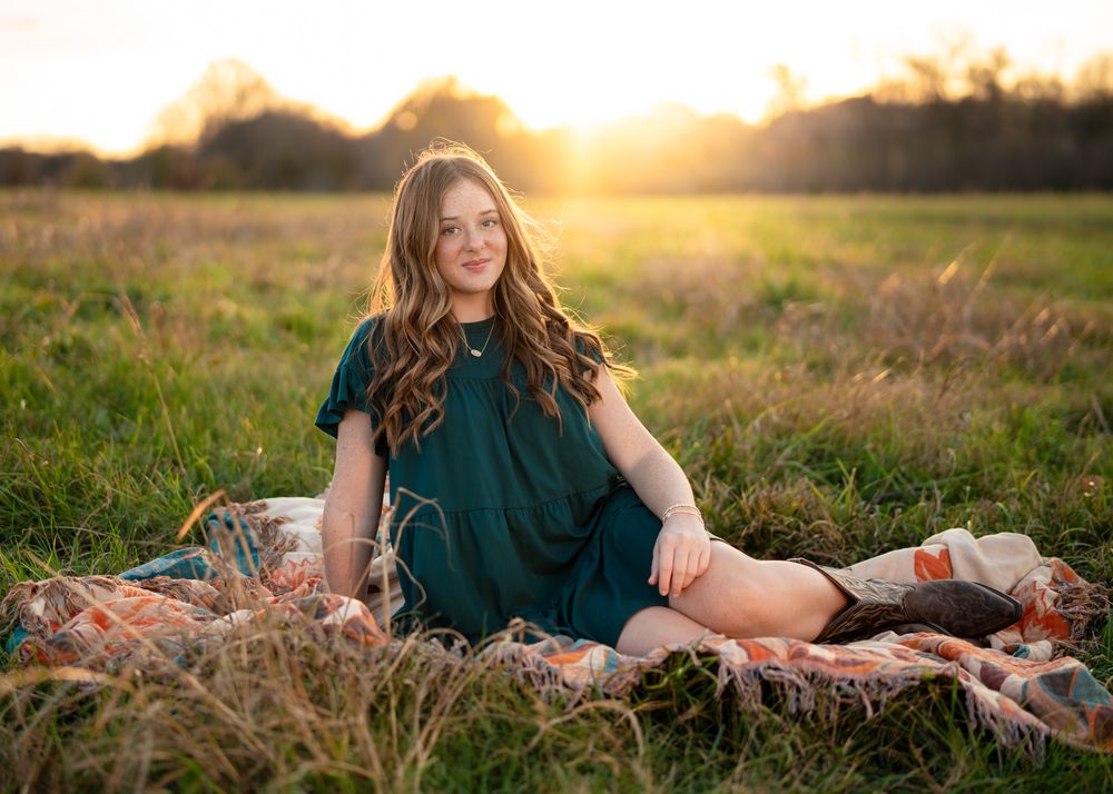 Golden sunset illuminates a grassy field with someone relaxing in casual attire during a warm evening photo session.