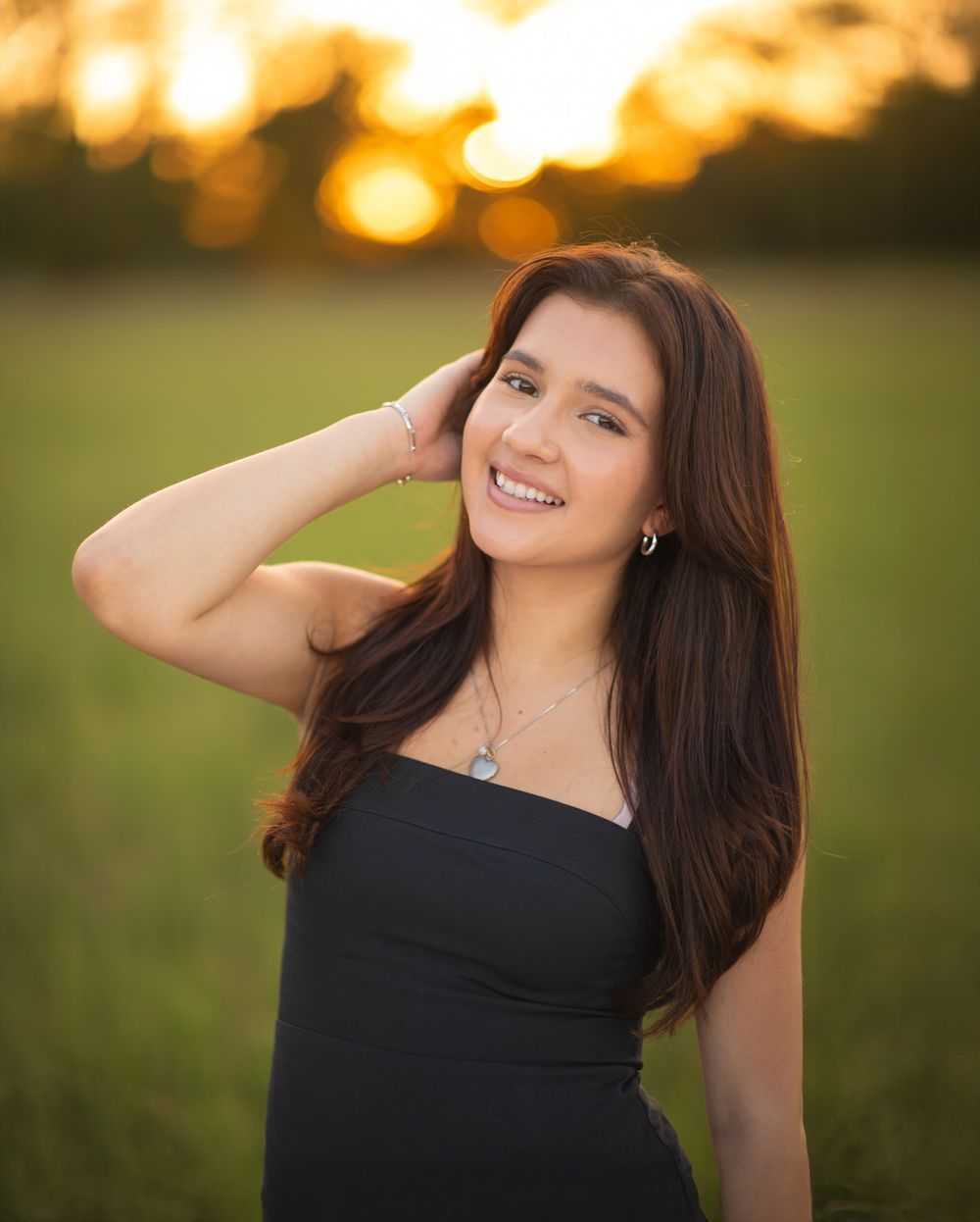 Portrait of someone in a black dress smiling warmly at sunset with golden bokeh lights in the background.