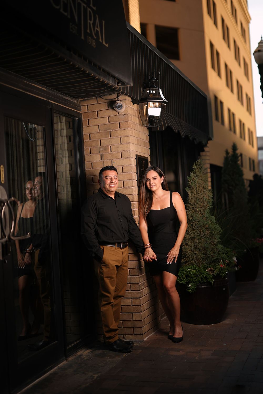 A couple poses together outside a brick building at dusk with dramatic evening lighting.