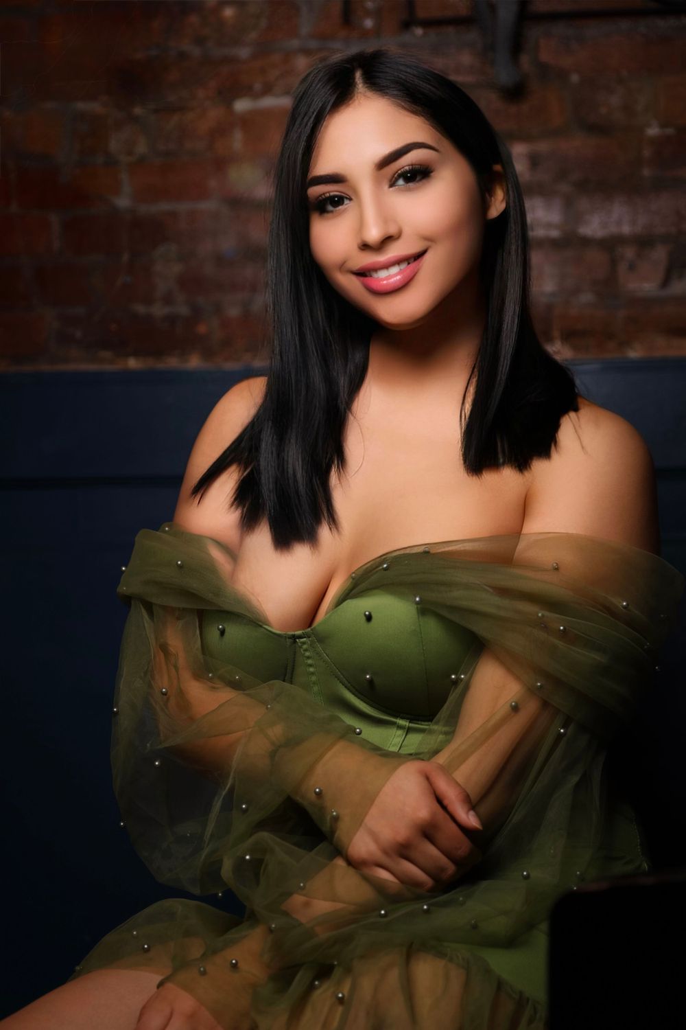 Portrait in olive green sheer dress against exposed brick wall with dramatic studio lighting.