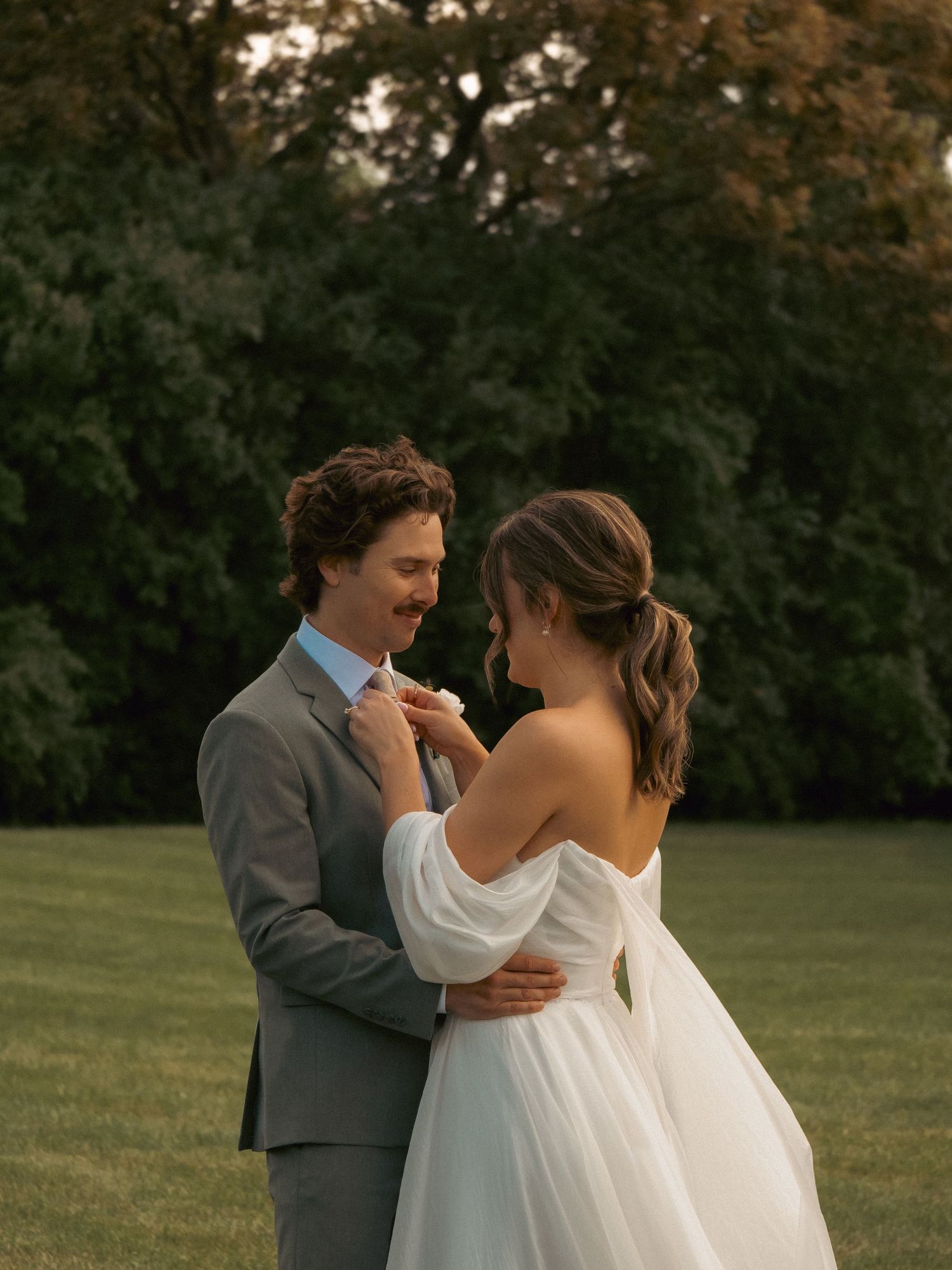 A couple shares an intimate dance moment on a lawn at sunset.