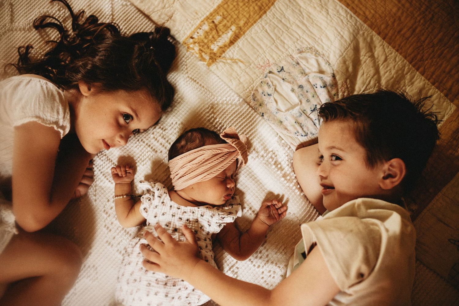 Brother and sister are lying down with their new sibling between them