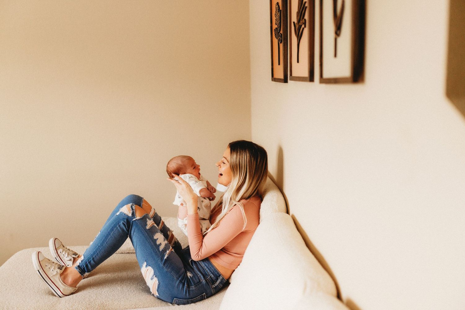 Mother is sitting on the couch smiling at her newborn
