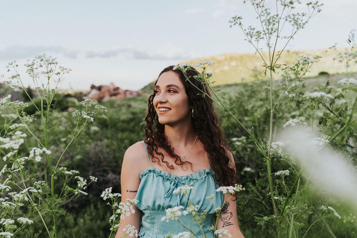 pregnant woman stands in knee-high creek water surrounded by green grasses