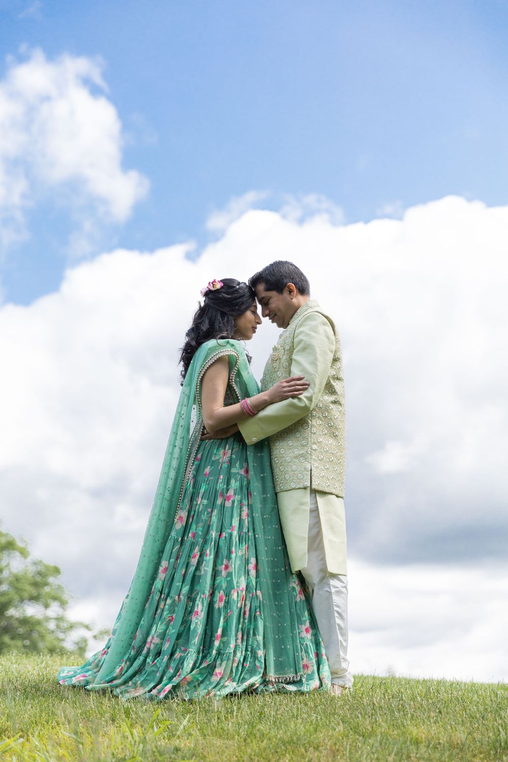 A romantic moment captured between a couple in mint green and cream traditional outfits on a hilltop.