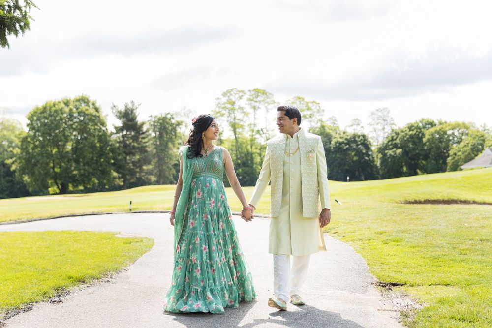 A couple in elegant South Asian attire walking together on a paved park path.