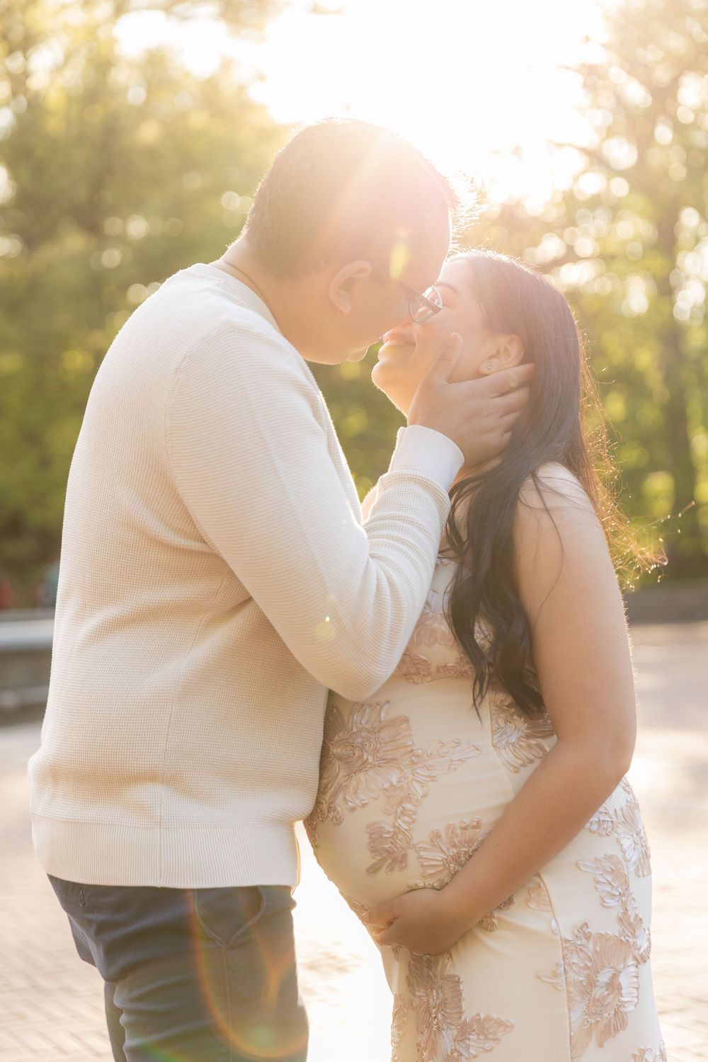 Couple sharing a tender moment in golden sunlight, man gently holding womans face as they lean in for a kiss outdoors.