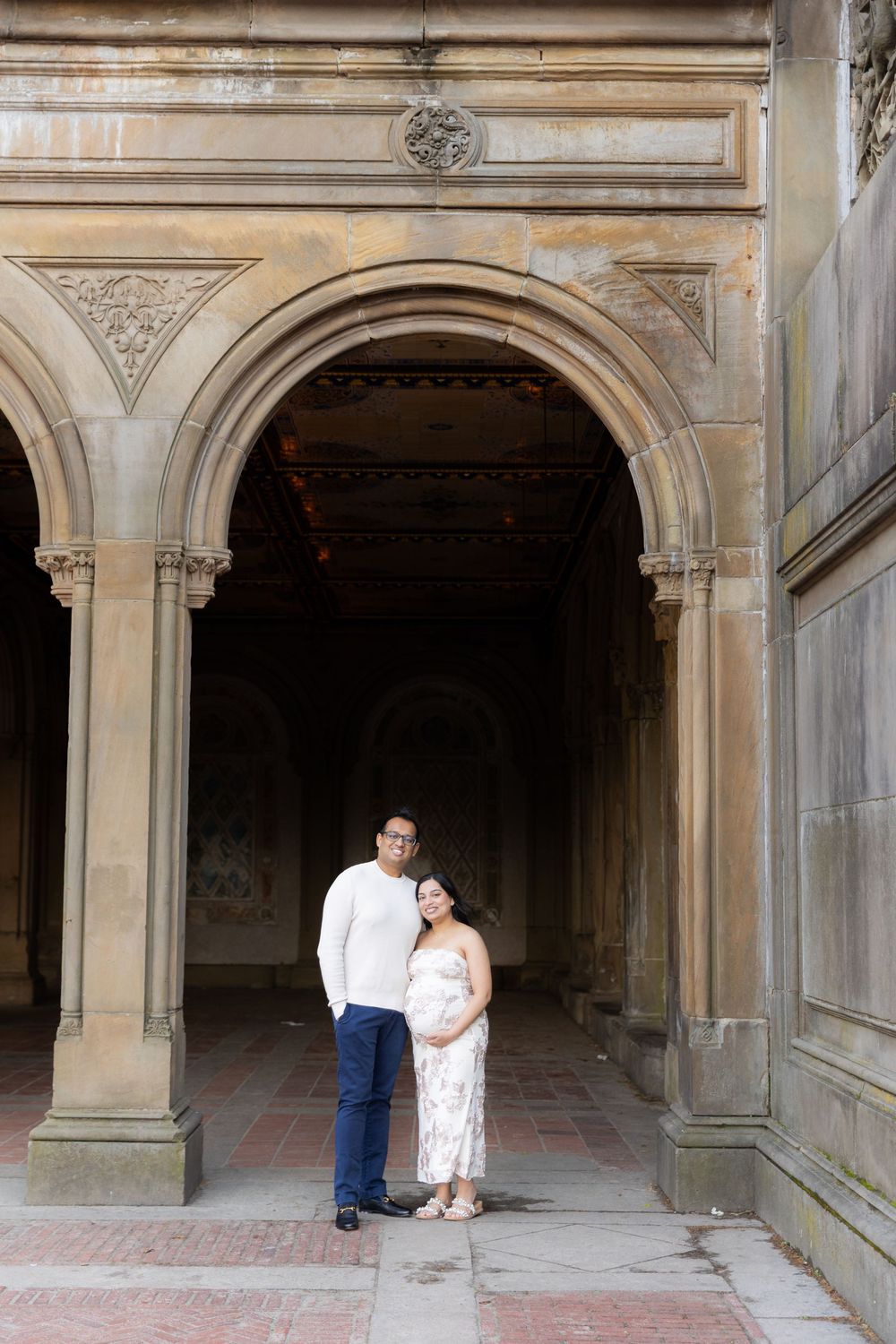 Couple poses under ornate stone arches at Bethesda Terrace in Central Park, New York City.