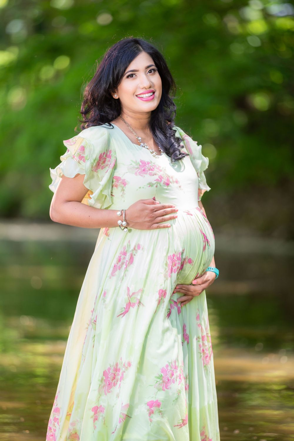 A floral mint green maternity dress flows elegantly against a natural forest backdrop.