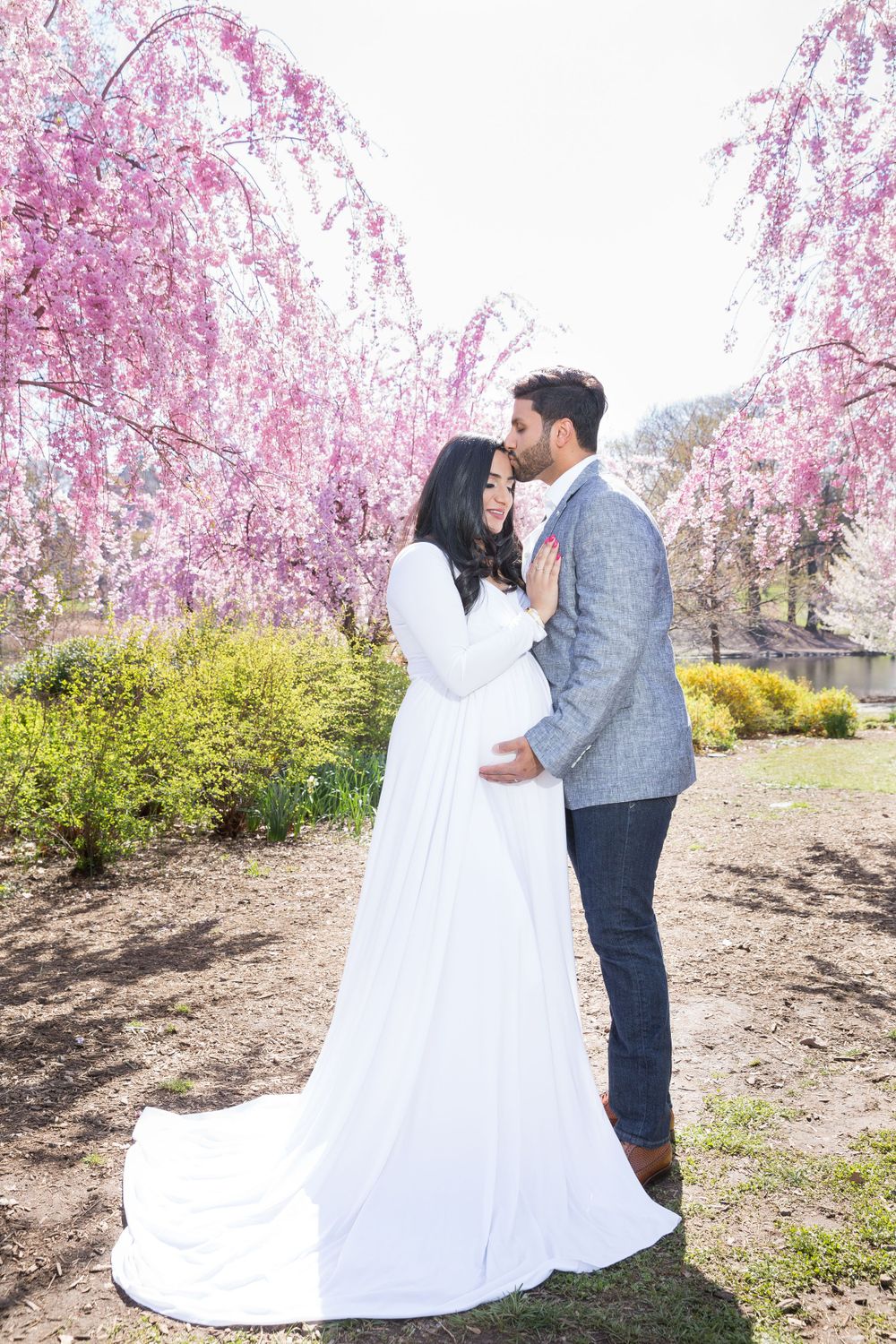 Wedding couple poses under blooming pink cherry blossom trees in spring garden.