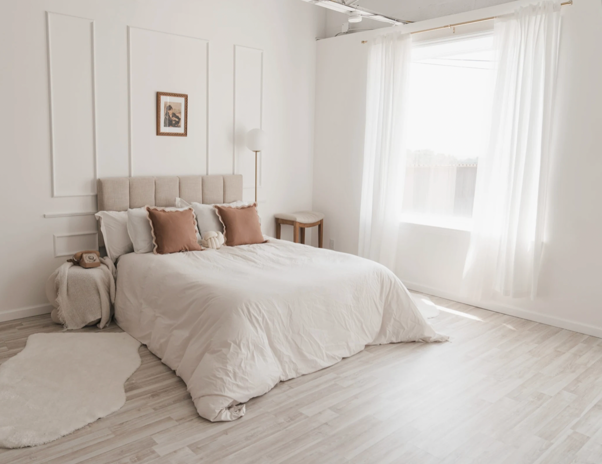 A serene bedroom with white bedding, blush accents, and elegant wall molding details.