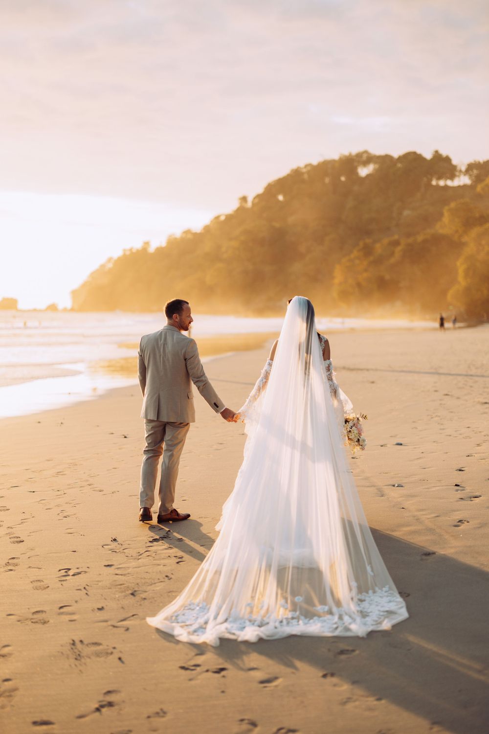 A couple walks hand in hand on a beach during golden hour.