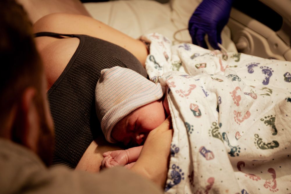Close-up of newborn baby being held against mother's chest in hospital.