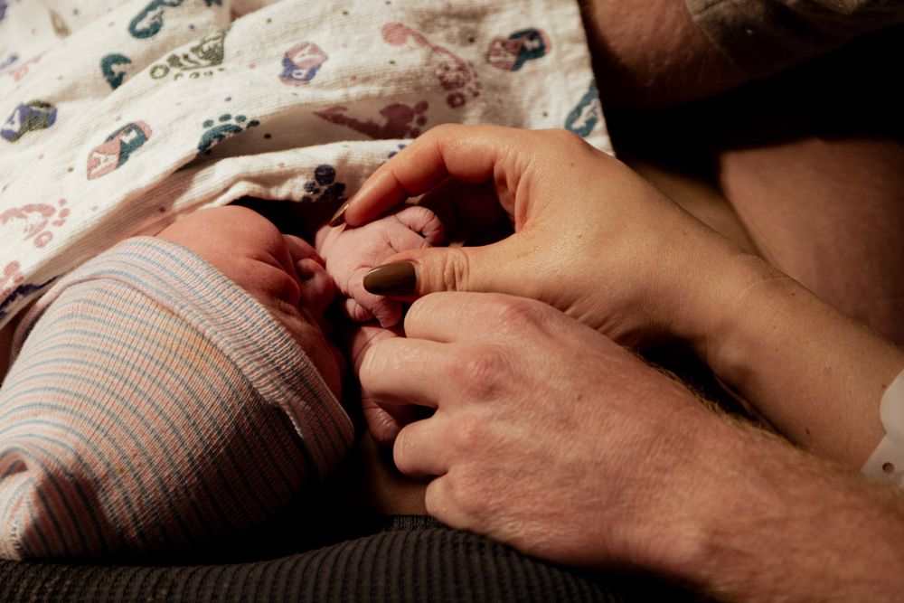 Gentle hands examining newborn baby wrapped in patterned hospital blanket.