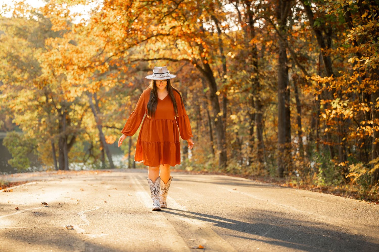 Woman in orange dress walking on autumn path surrounded by golden leaves.